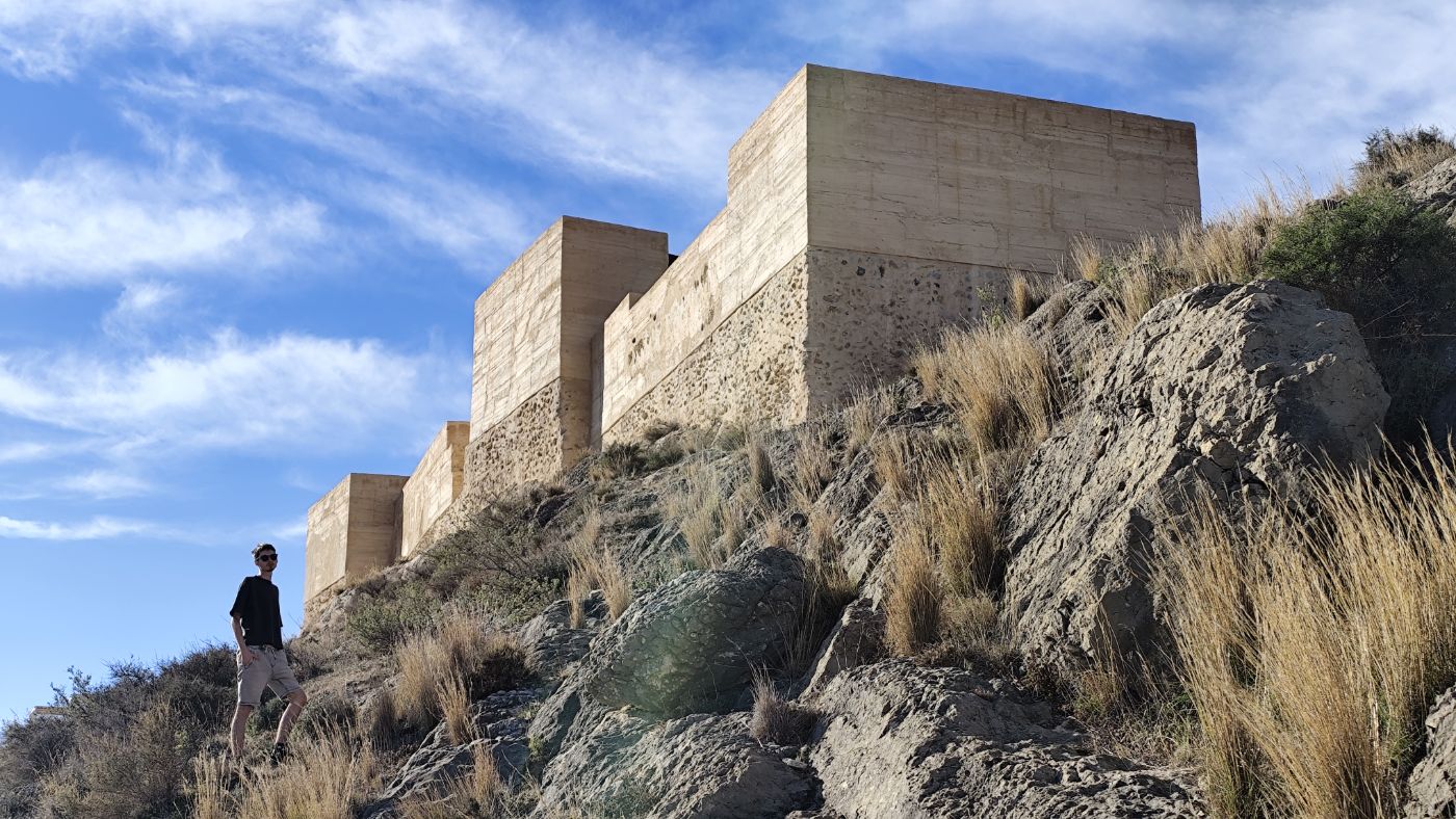 Walking below concrete fortress walls on a dry hillside