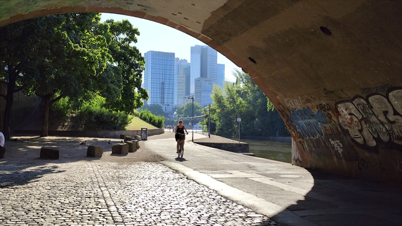 A cyclist under a bridge arch, skyscrapers behind