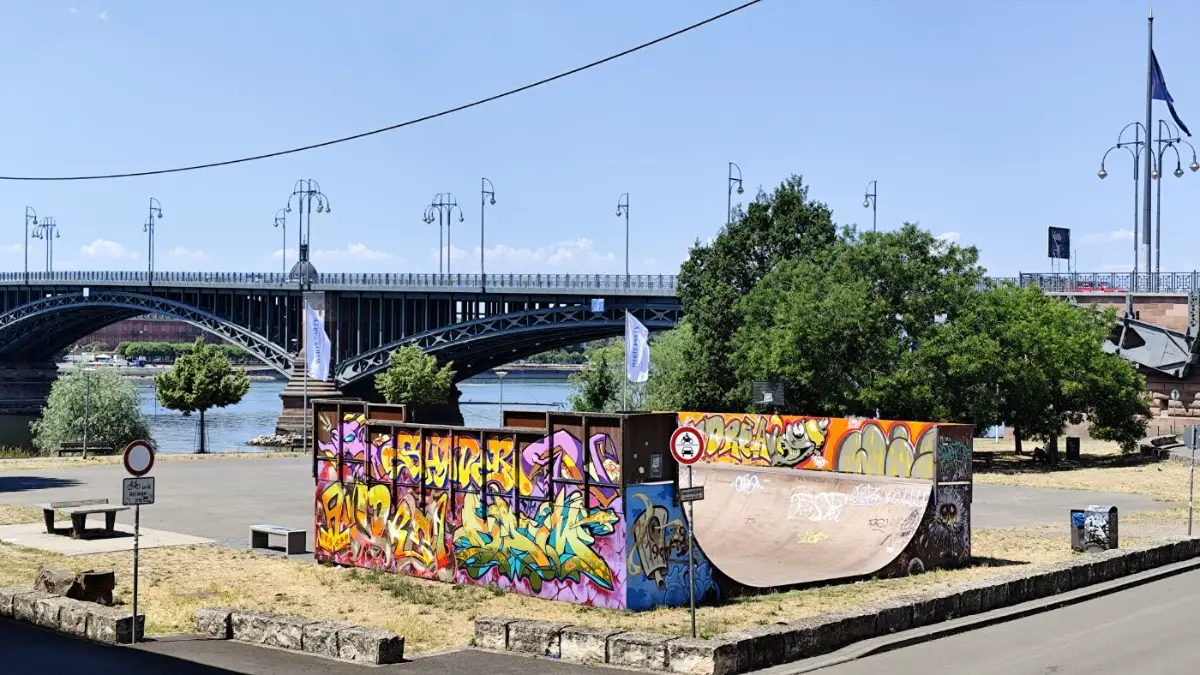 A graffiti skate ramp by a river bridge