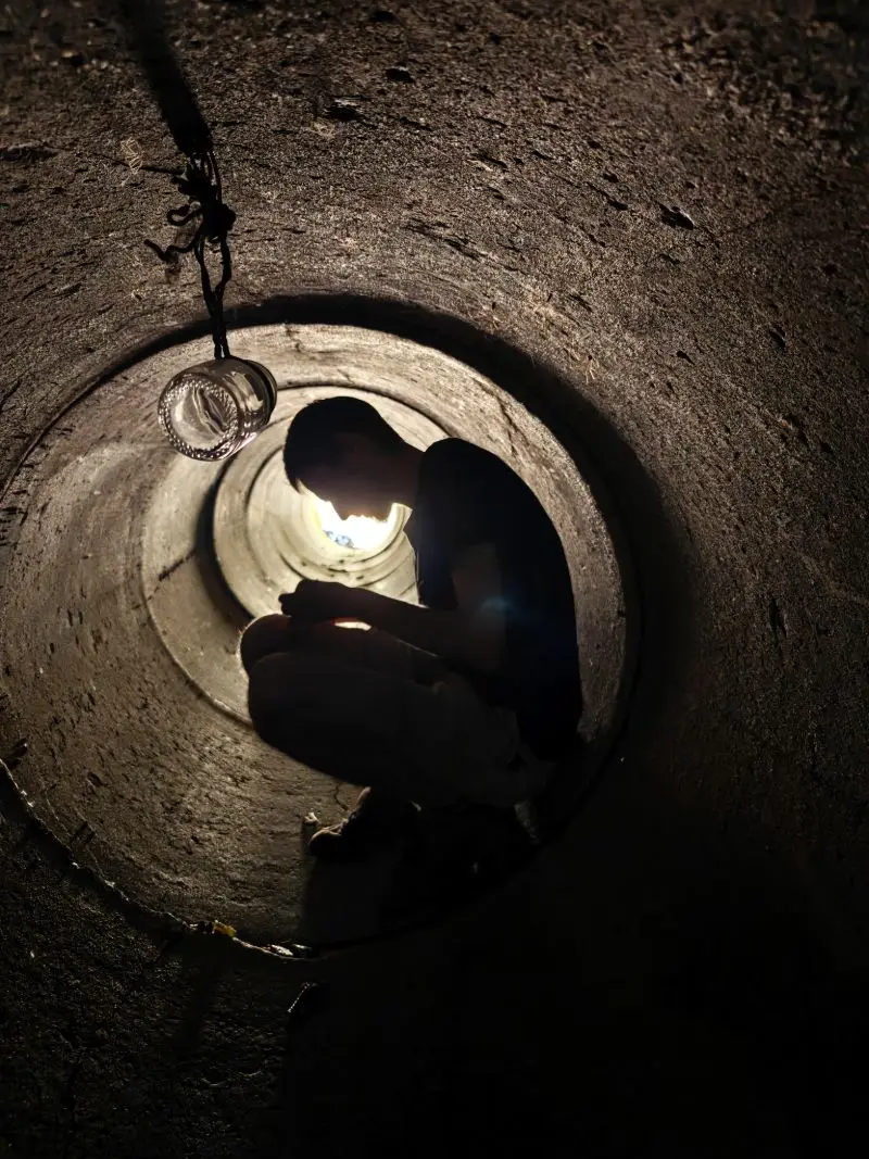 Silhouette crouching inside a concrete pipe